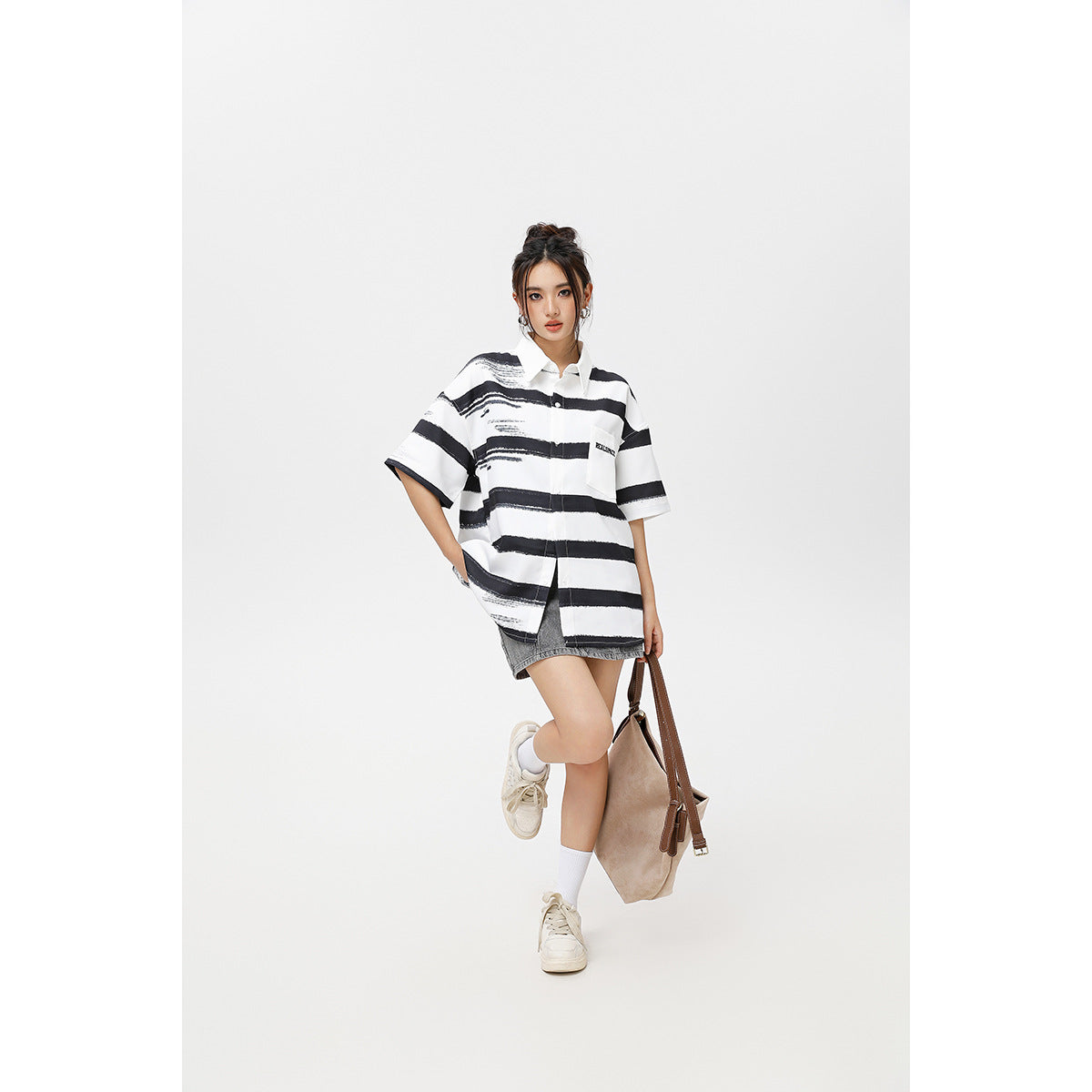 Model wearing an oversized white shirt with black brushstroke stripes, a gray denim skirt, white socks and sneakers.