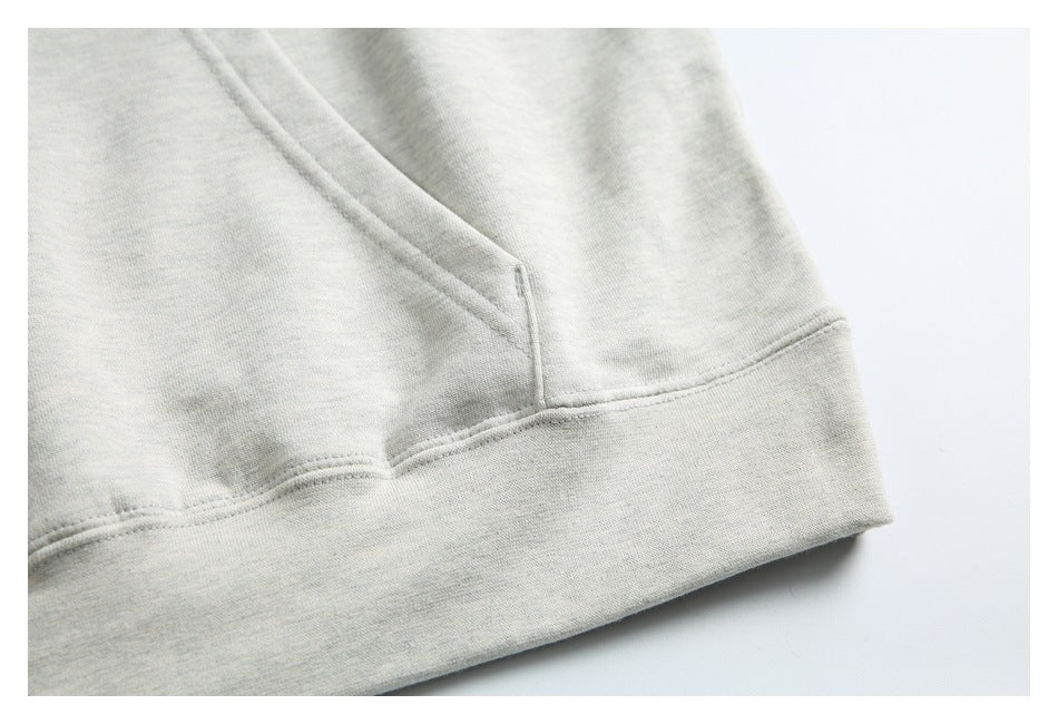 Close-up of the kangaroo pocket opening and ribbed hem on a light gray hoodie.