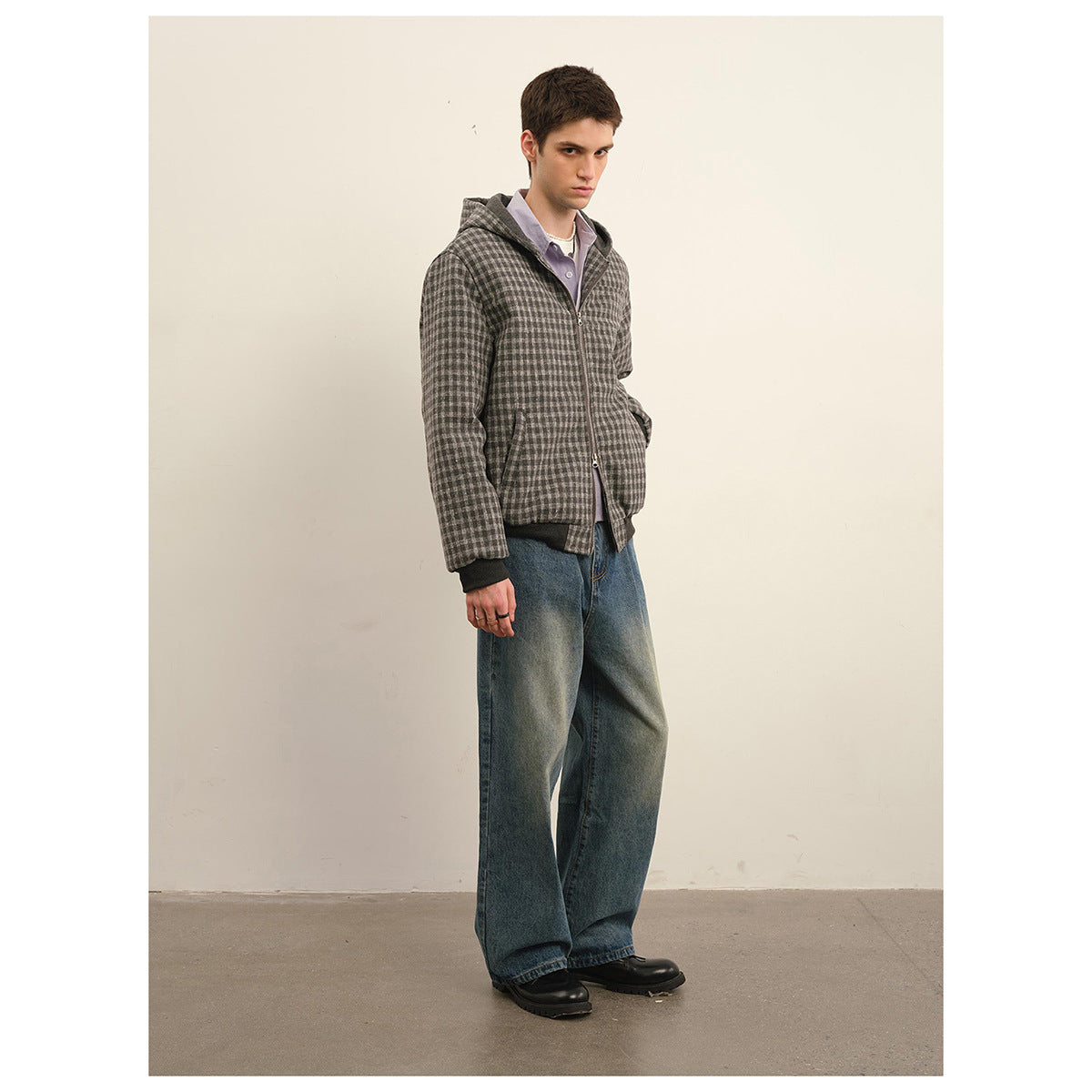 Model wearing a gray check hooded zip jacket with dark ribbed trim and loose blue jeans.