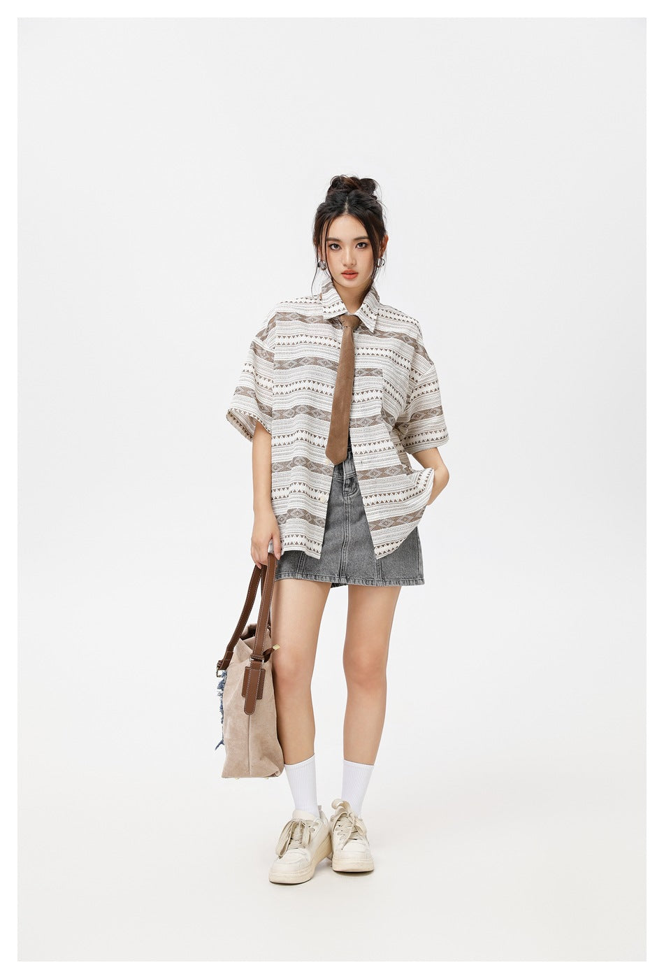 Model wearing an oversized taupe geometric short-sleeve shirt with a brown tie and gray denim mini skirt.