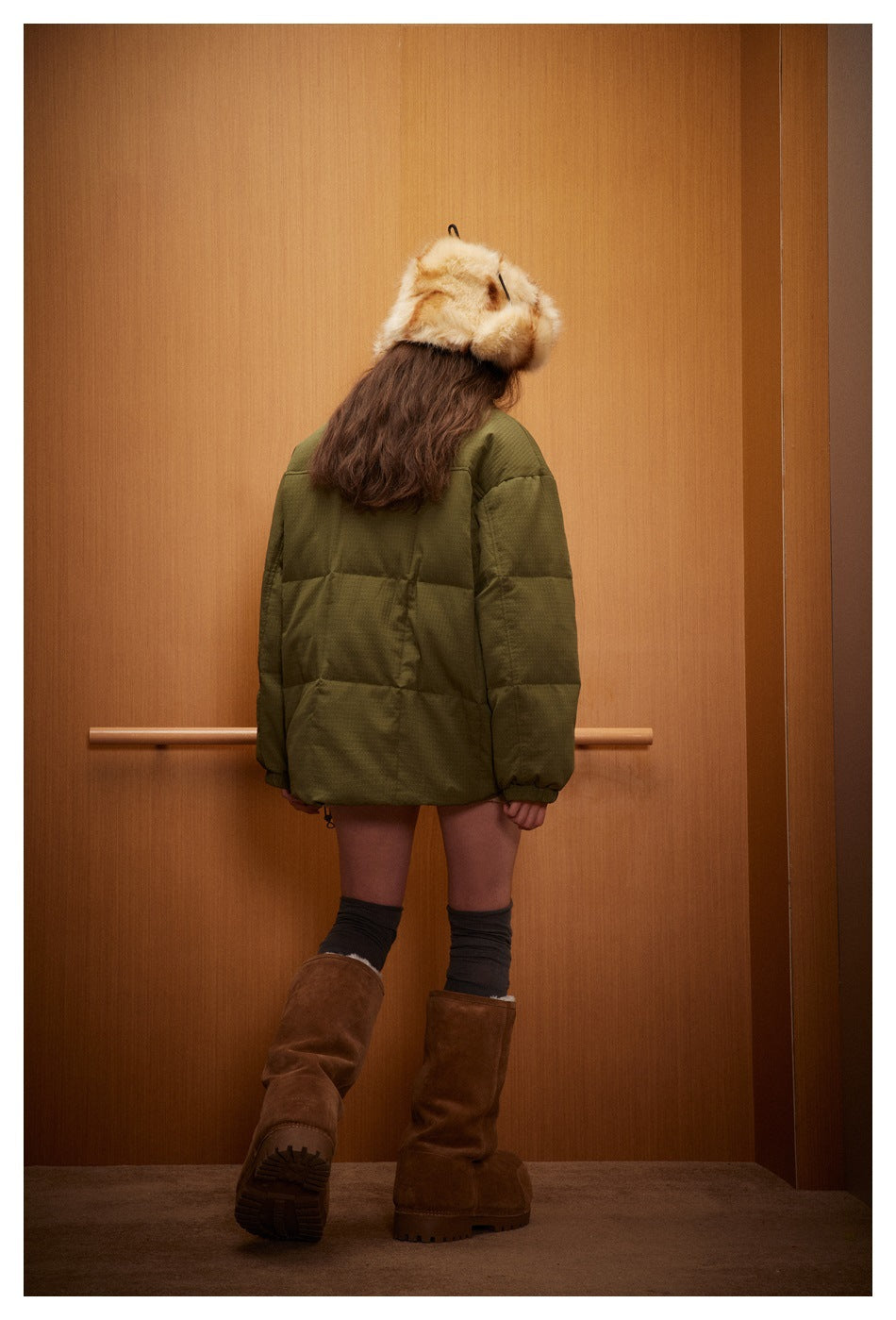 Rear view of a model wearing an olive quilted jacket with a wide, segmented back and elastic cuffs.