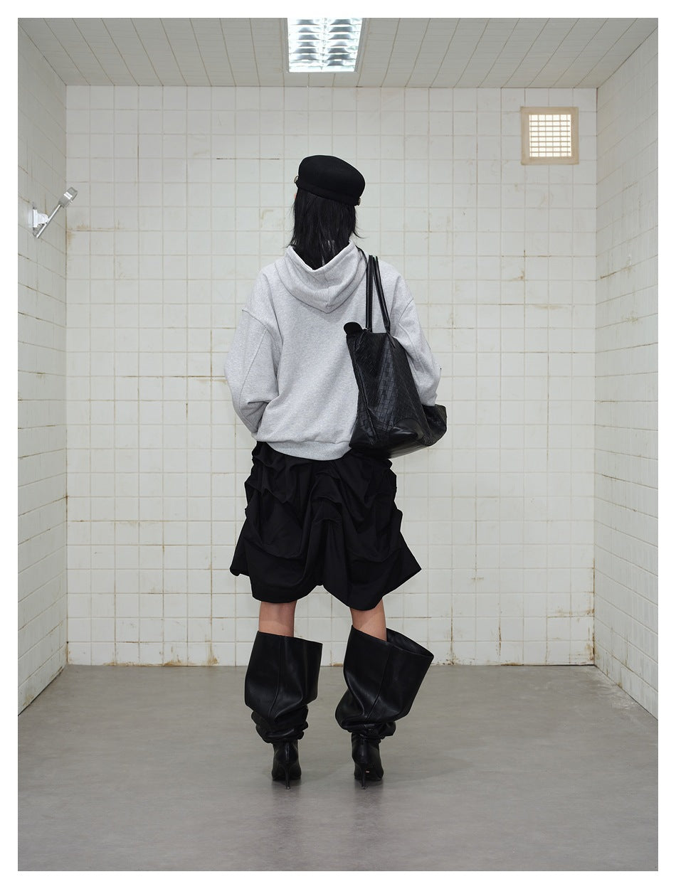 Back view of a model in a plain gray hooded sweatshirt, layered black skirt, and tall black boots.