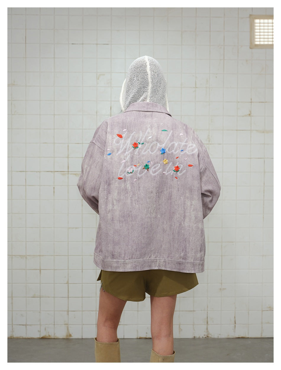 Back view of a model wearing a dusty mauve jacket with large floral script embroidery and olive shorts.