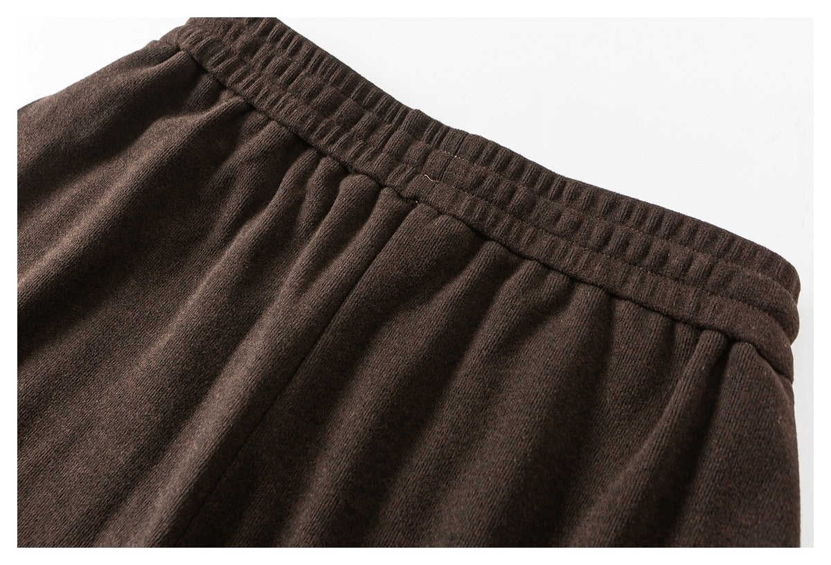 Close-up of the gathered elastic waistband and pleated front of dark brown pants.