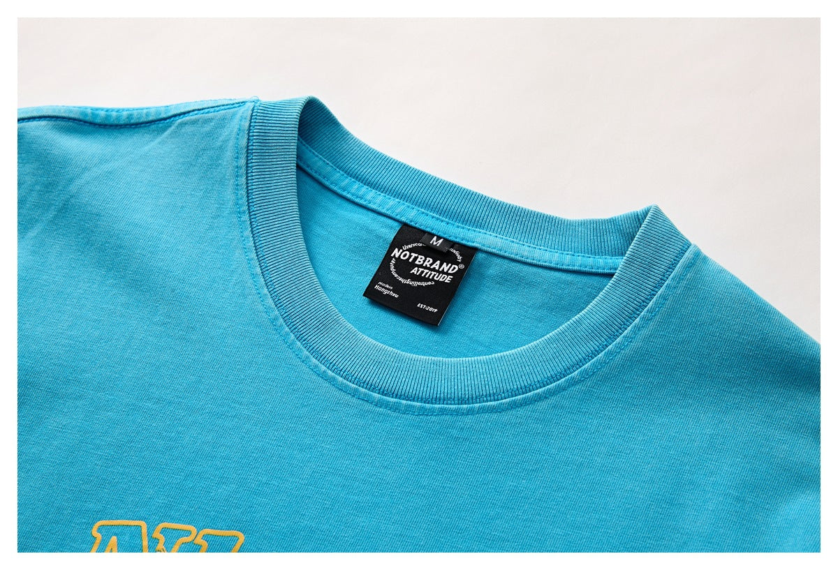Close-up of a turquoise T-shirt's ribbed crew neck, black neck label and partial yellow chest print.