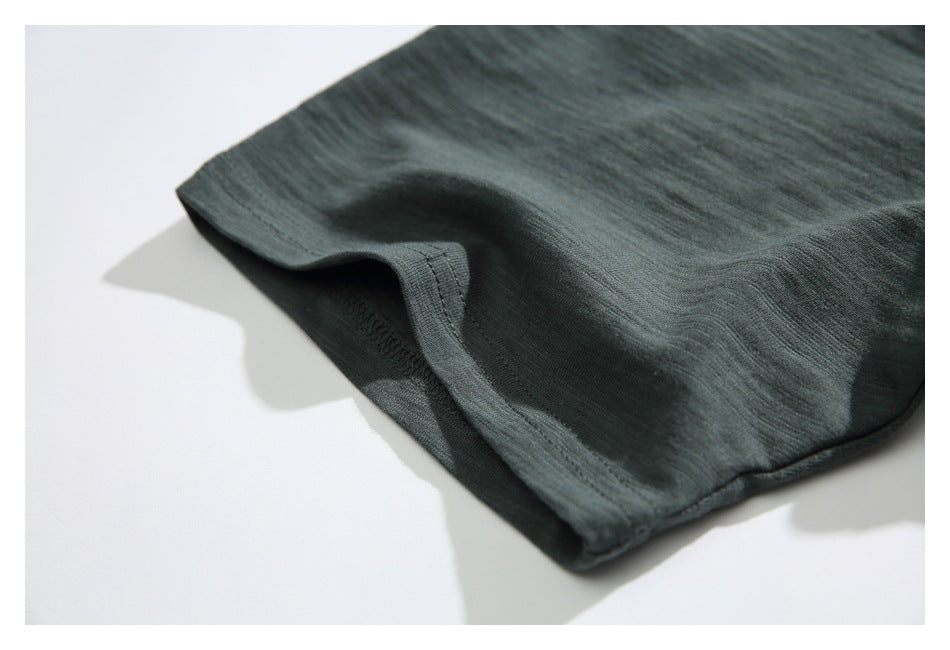 Close-up of the dark green shirt sleeve hem and stitched edge against a white background.