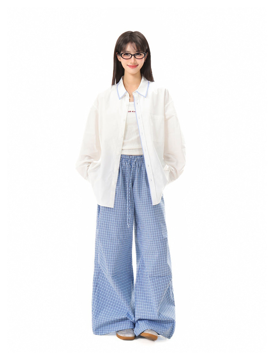 Smiling model with hands in pockets wearing an open white striped-trim shirt, tank top and blue plaid pants