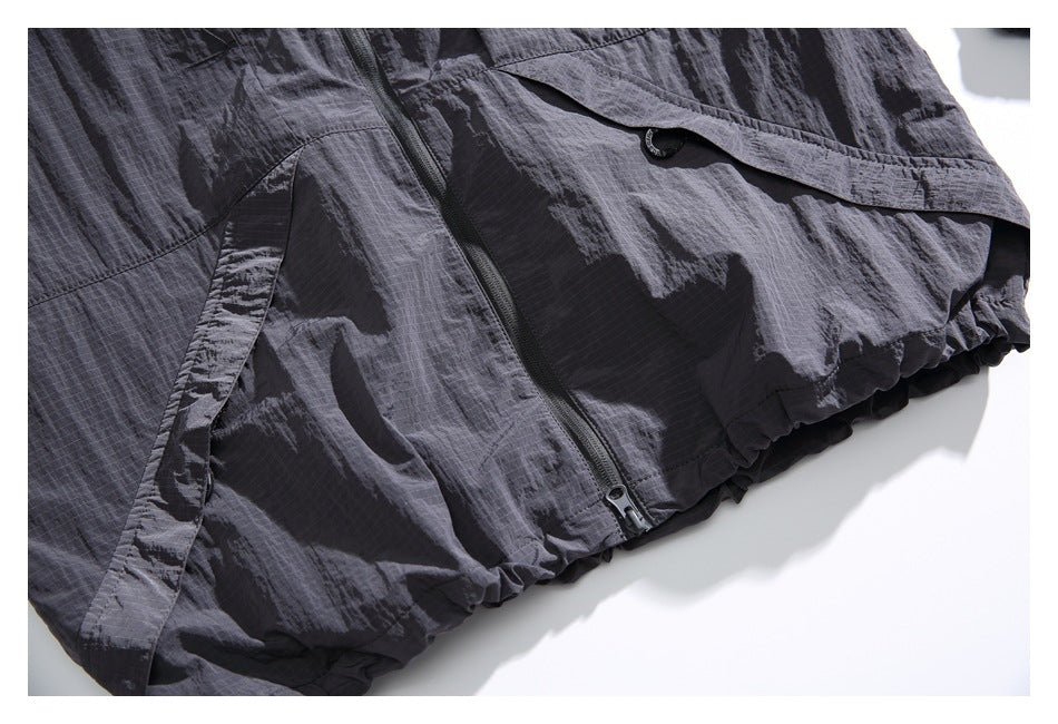 Close-up of the charcoal jacket’s front zipper, flap pocket, and gathered hem.