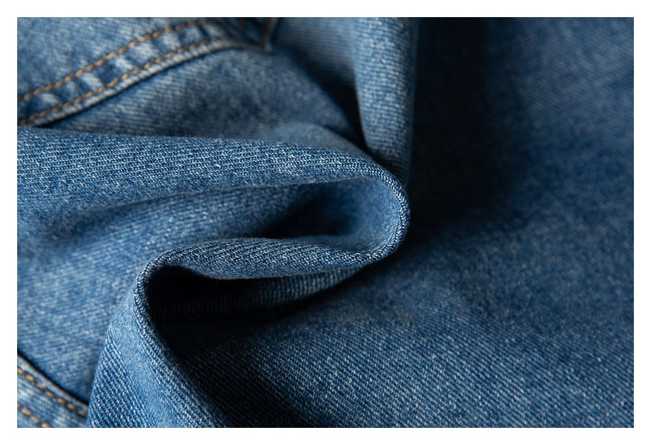 Macro view of blue denim fabric folded to show its weave, texture, and tan stitching.