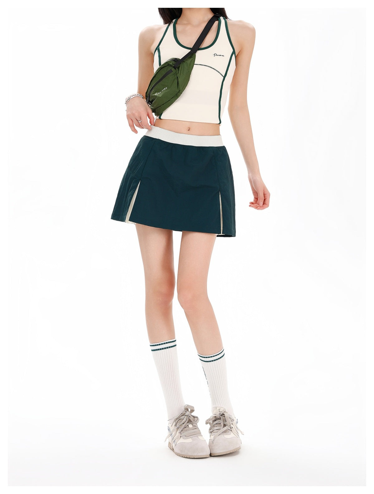 Front view of a model wearing a dark teal athletic skirt with a wide white waistband and contrasting side panels.