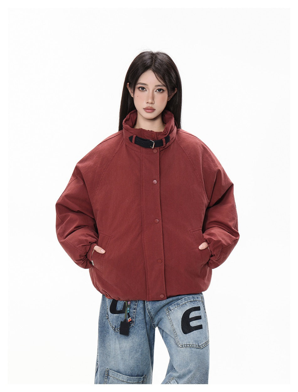 Close-up of model in burgundy stand-collar jacket with black collar strap, snap front and hands in pockets