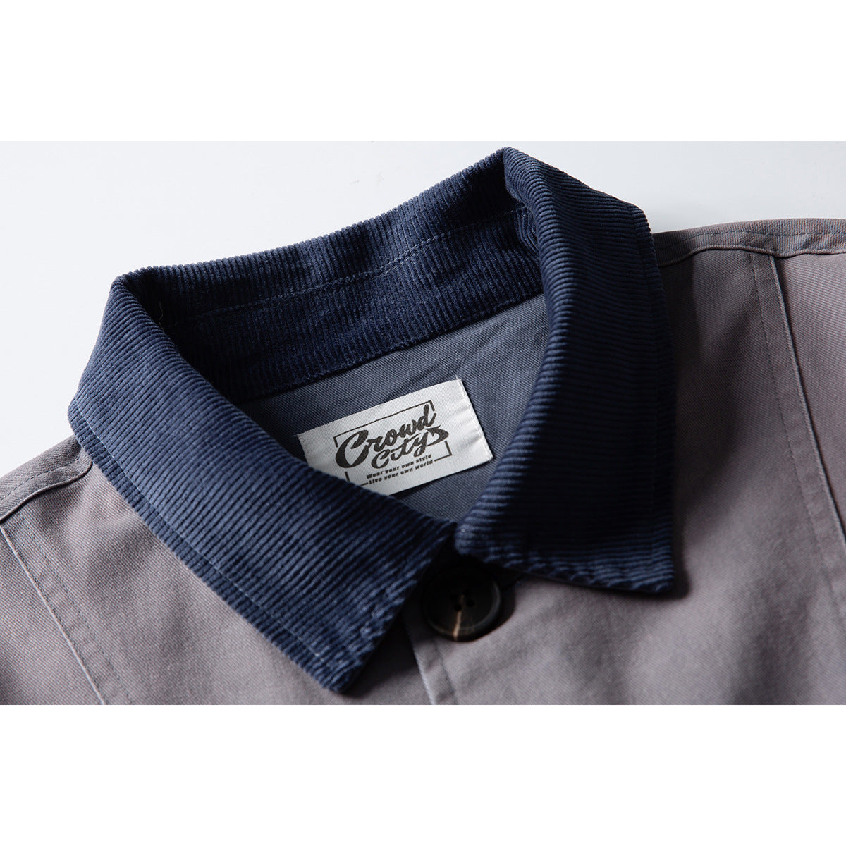 Close-up of a gray jacket’s dark navy ribbed collar, button, and sewn neck label.