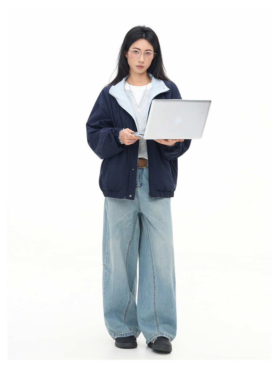 Model wearing a navy jacket with light blue striped collar, gray top and wide-leg light wash jeans, holding a laptop
