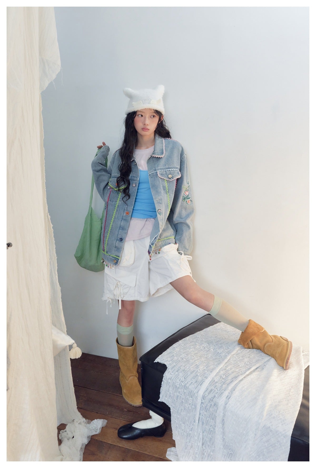 Full-length model wearing a decorated light-blue denim jacket, white cargo shorts and tan boots.