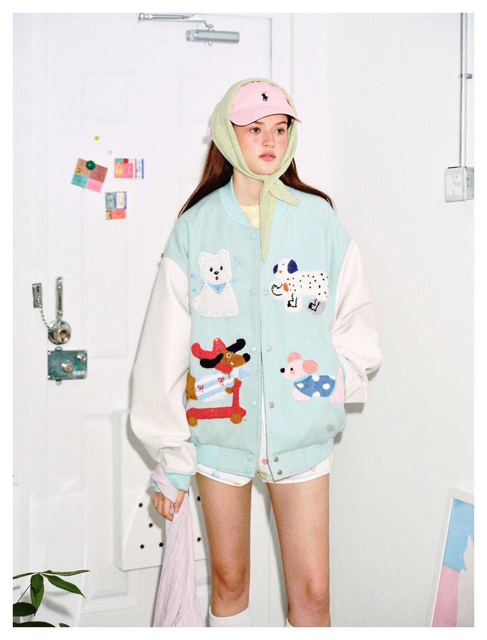 Model wearing a pale aqua varsity jacket with white sleeves and animal appliqués, with a pink cap and pale green headscarf.