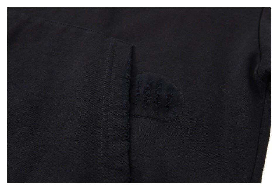 Close-up of a black hoodie pocket edge and a small distressed fabric patch.