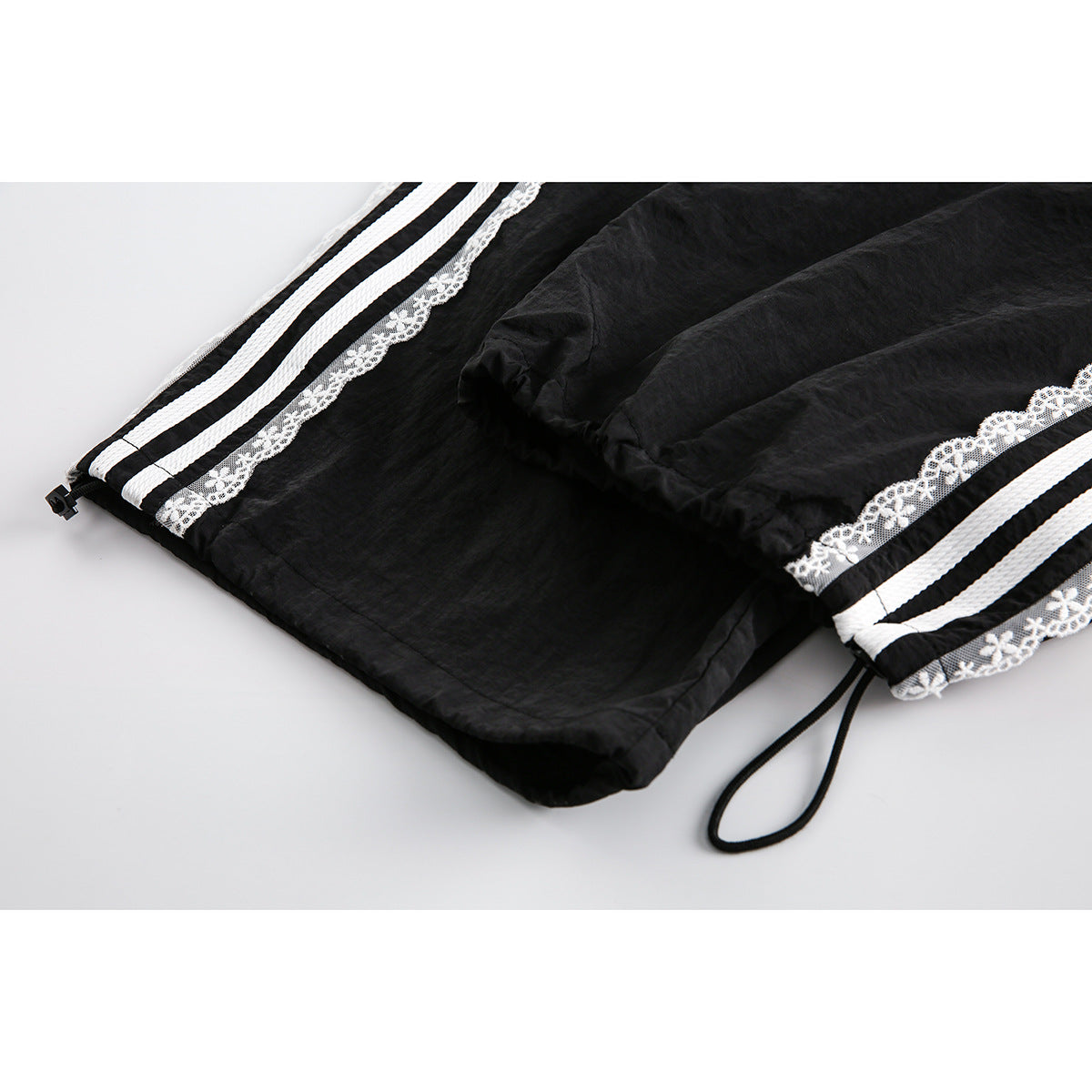 Close-up of the black pants' lower legs, showing white side stripes, floral lace, and drawcord hems.