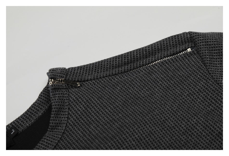 Close-up of a dark charcoal textured garment with a zipper along the edge and a small T label.