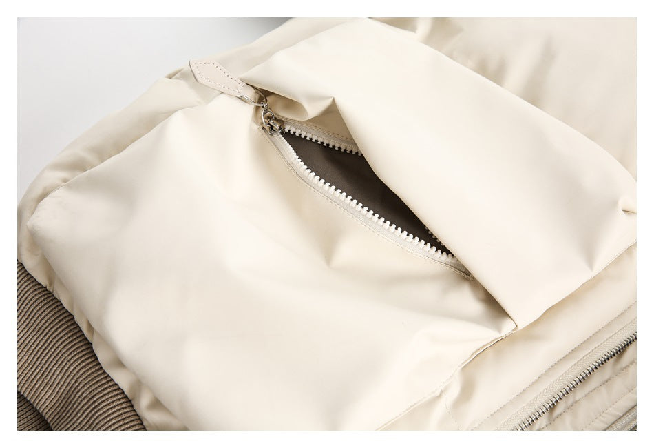 Close-up of a cream jacket pocket with a partially open zipper and taupe ribbed trim.