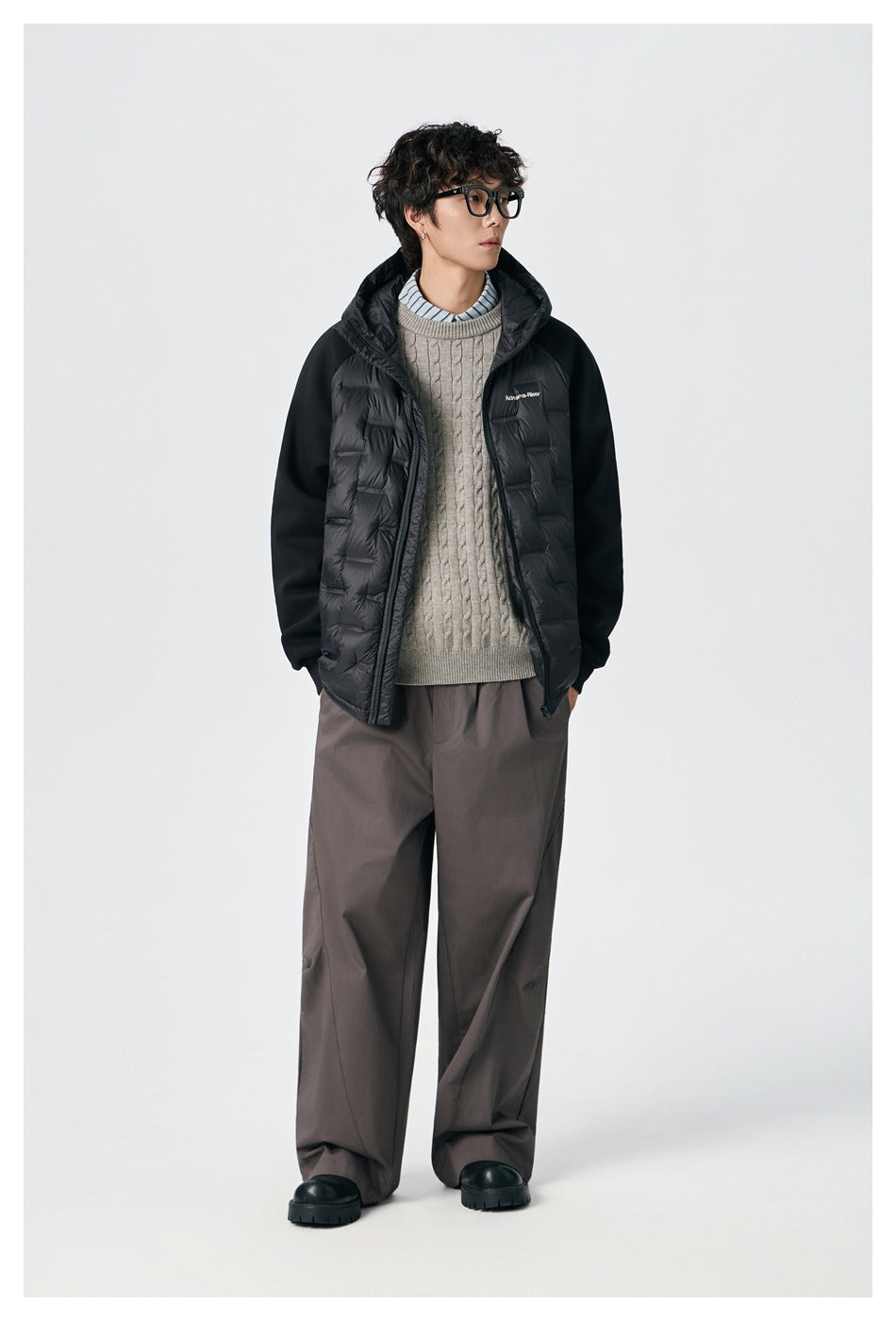 Full-length model wearing a black hooded jacket with quilted front panels and contrasting sleeves.