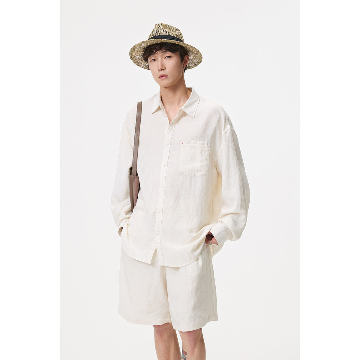 A standing man models an off-white button-up shirt and matching shorts with a woven straw hat.