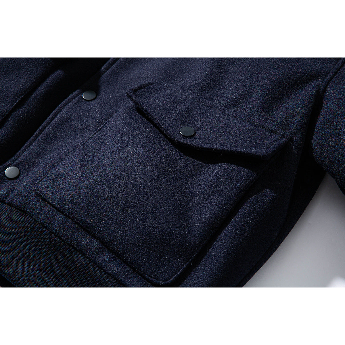 Close-up of a dark navy jacket showing a flap pocket, snap buttons, and ribbed hem.