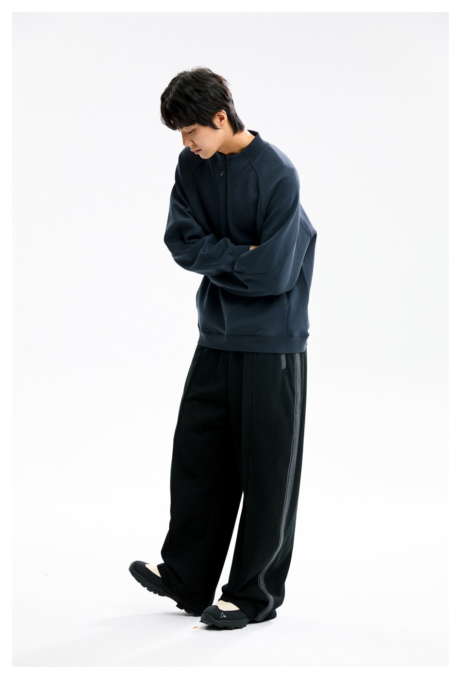 Model in a dark navy quarter-zip sweatshirt and black wide-leg pants, shown standing with arms folded.