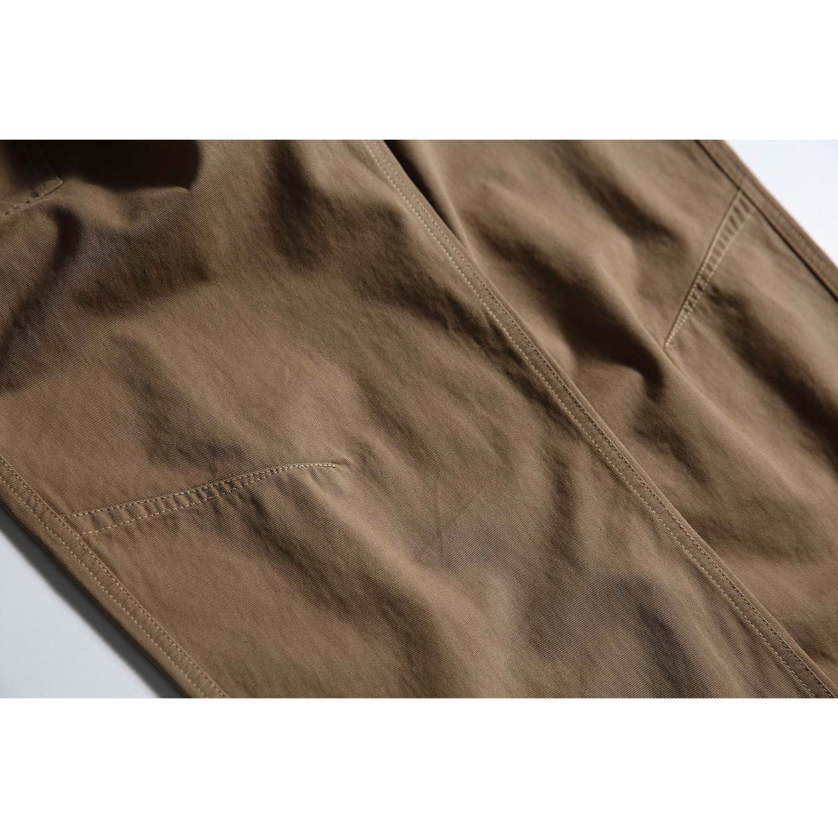 Close-up of brown pants showing a stitched leg seam and panel detailing.