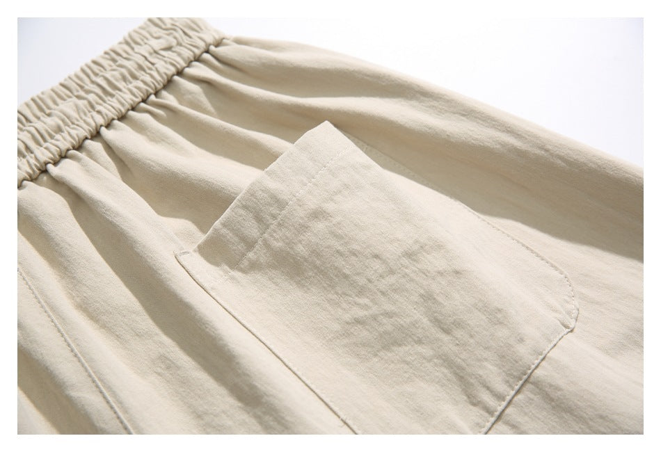 Close-up of a large patch pocket and gathered elastic waistband on beige pants.