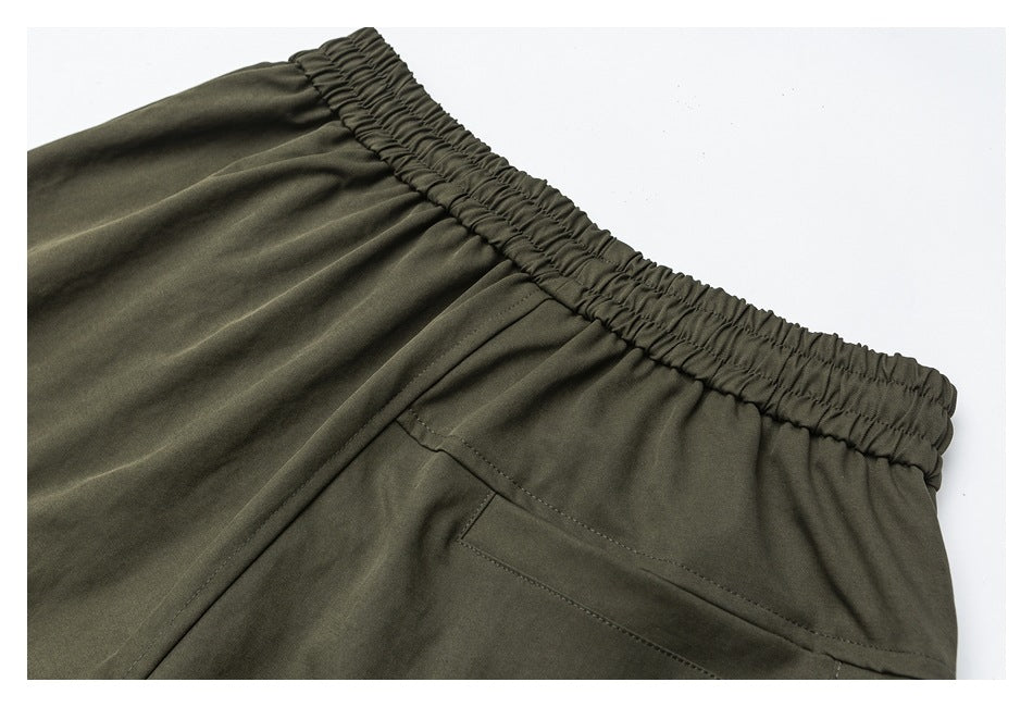 Close-up of olive trousers showing a gathered elastic waistband and slanted pocket.