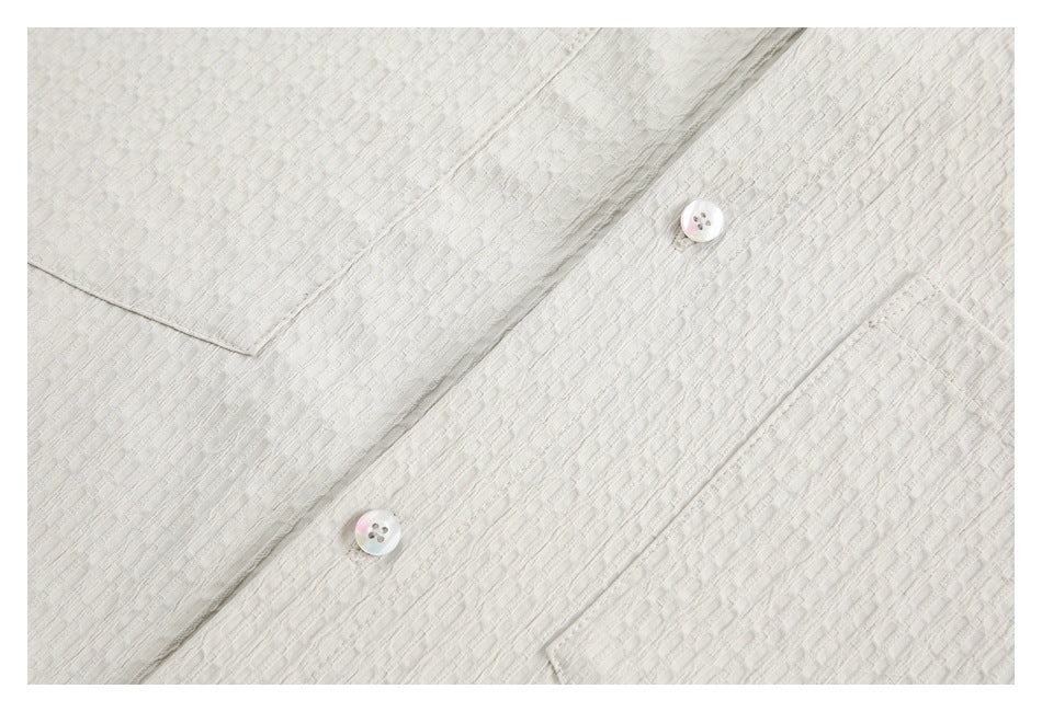 Close-up of the ivory shirt's textured fabric, button placket, and iridescent buttons.