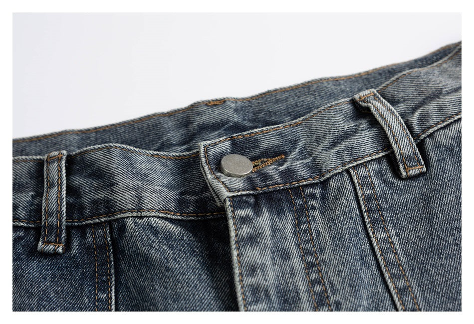 Close-up of washed blue-gray jeans showing the waistband, belt loops, metal button, and fly stitching.