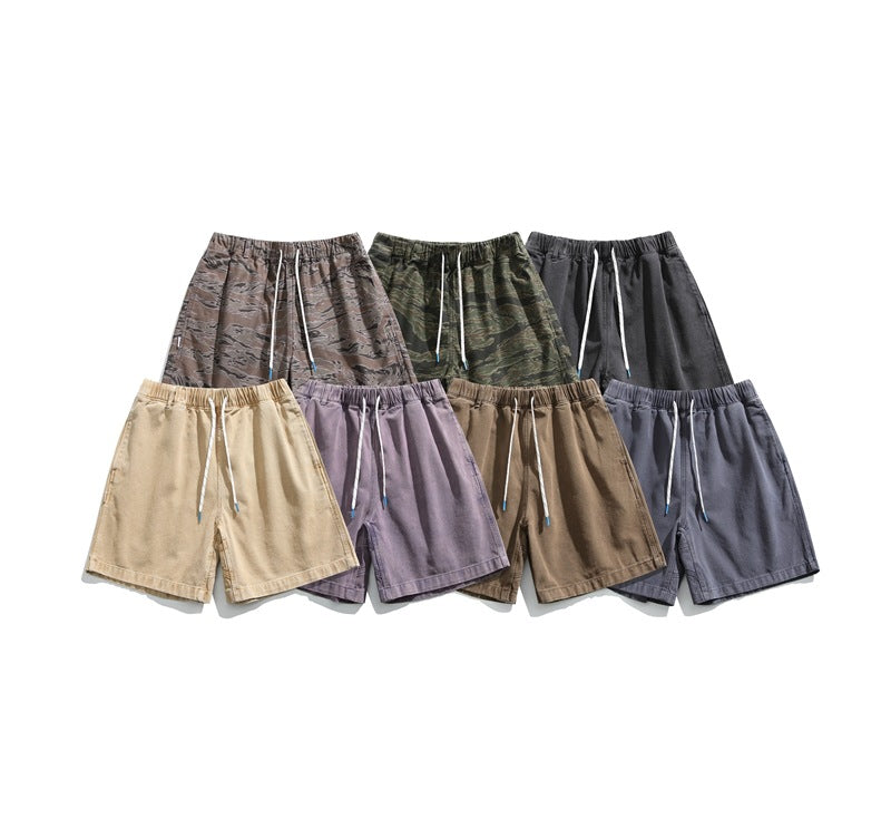 Seven pairs of loose drawstring shorts arranged in camouflage, charcoal, beige, mauve, brown, and slate colorways.
