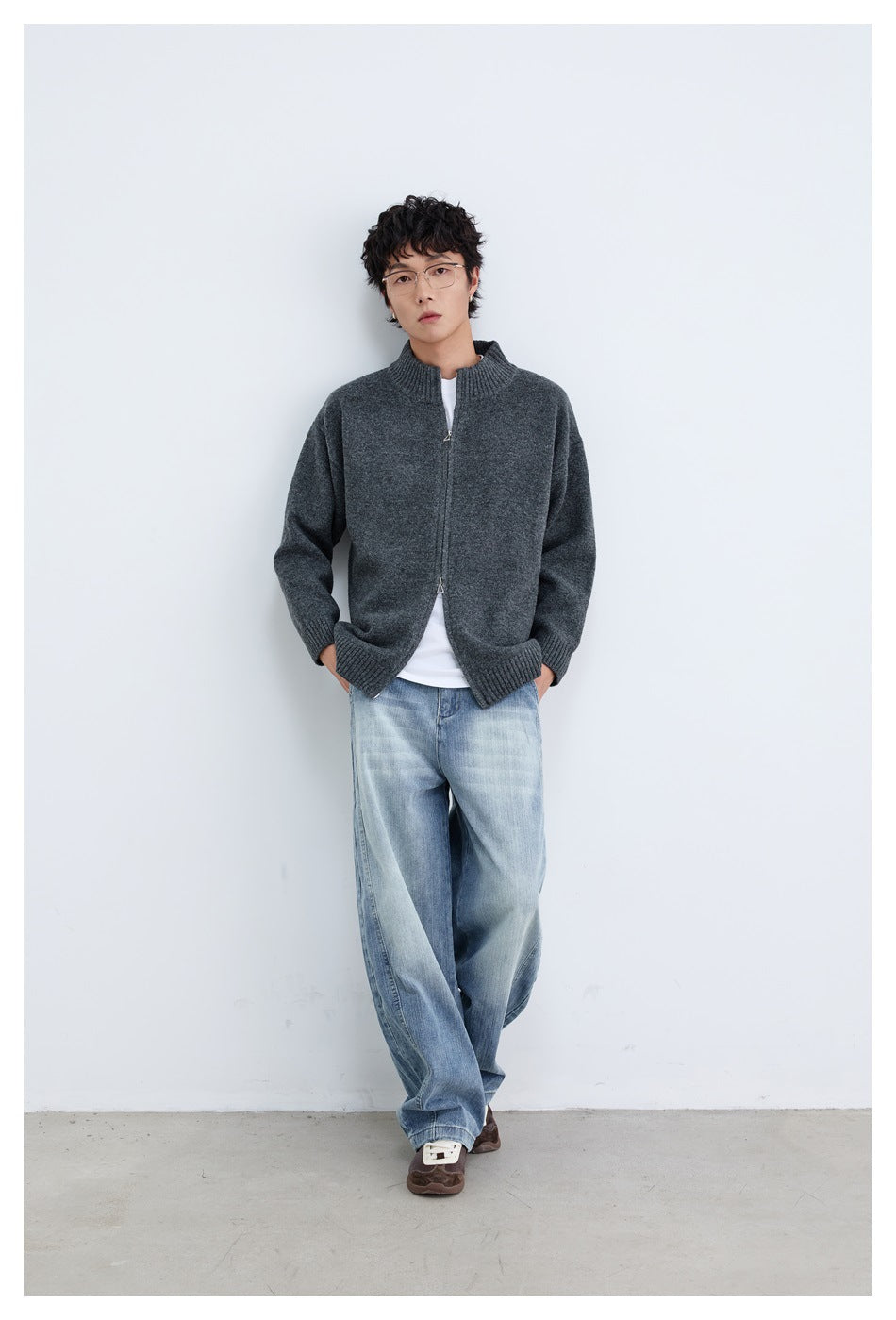 Model standing in a charcoal gray zip-front cardigan with ribbed trim, a white shirt and loose light-wash jeans.