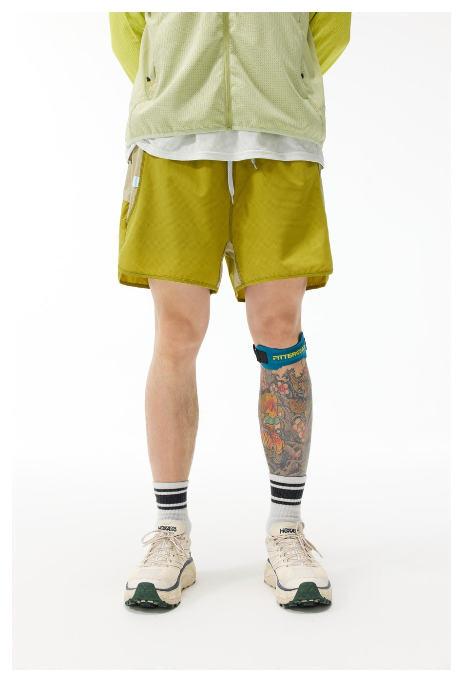 Front view of a model wearing mustard yellow athletic shorts with a drawstring and a pale vest.