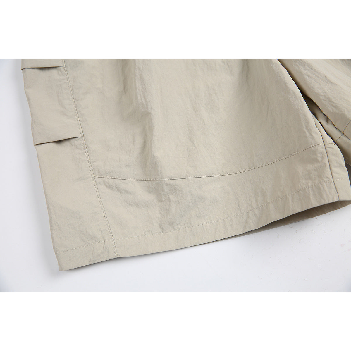 Close-up of beige shorts showing the lower hem and stitched side panels.