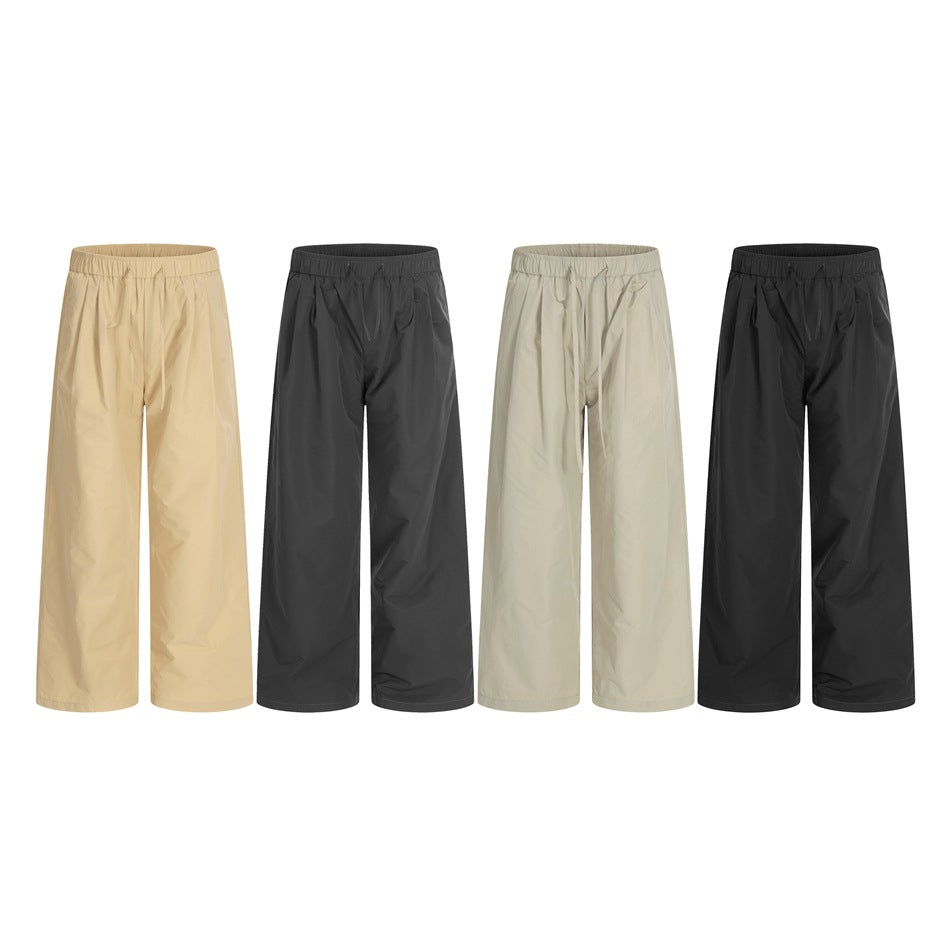 Four pairs of loose drawstring trousers shown side by side in beige, charcoal, pale sage, and black.