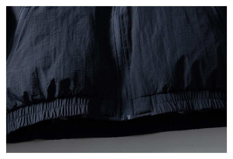 Close-up of the dark navy jacket's center-front zipper and elasticated hem.