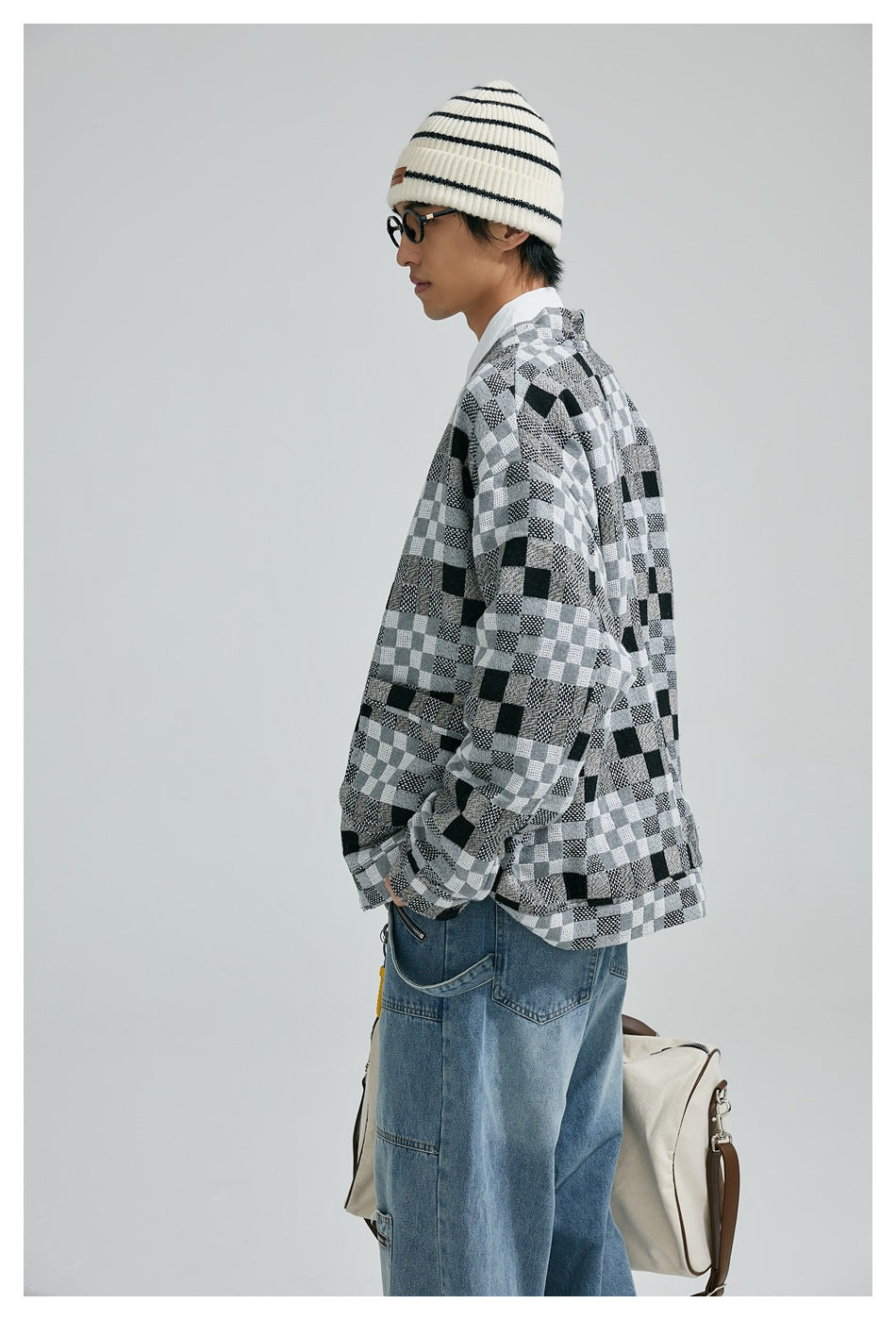 Model in a black, gray and white patchwork-check cardigan, shown in side profile with striped beanie and blue jeans.