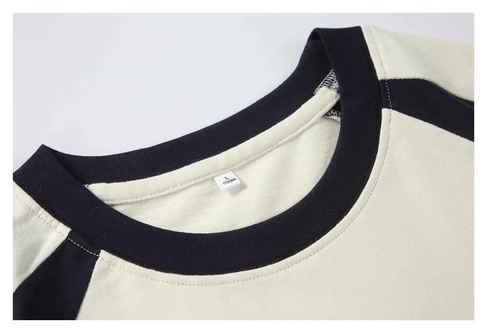 Close-up of the cream T-shirt's black ribbed neckline, raglan seam, and inner size label.