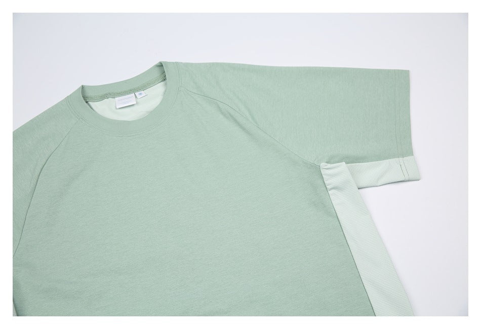 Close-up of the upper front of a sage-green raglan shirt, showing the crew neck, sleeve, and pale side panel.