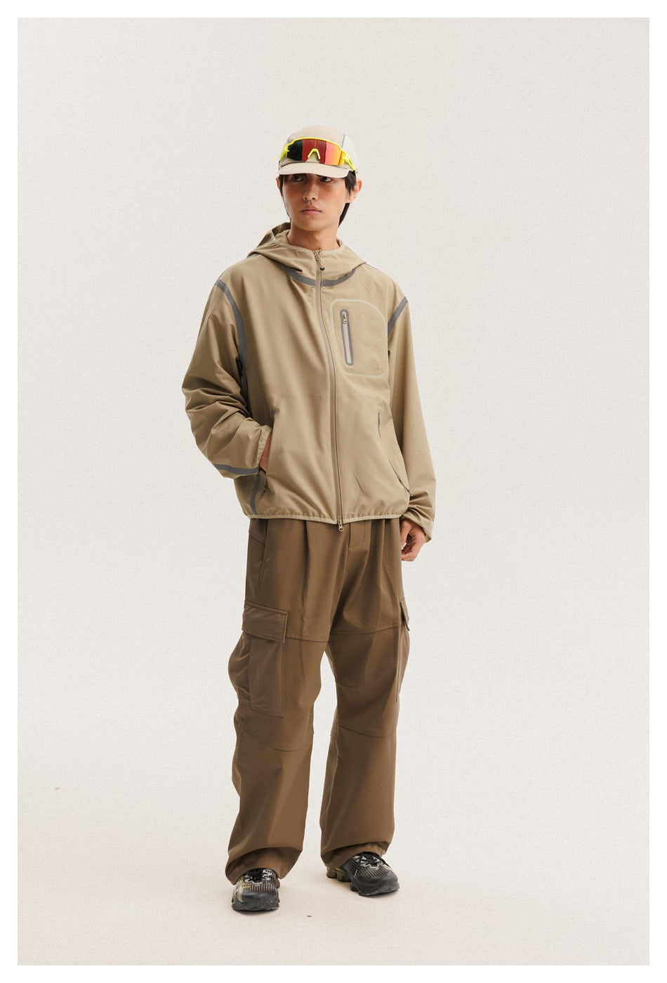 Model wearing a tan hooded zip jacket with gray trim and brown cargo pants, shown full length from the front.