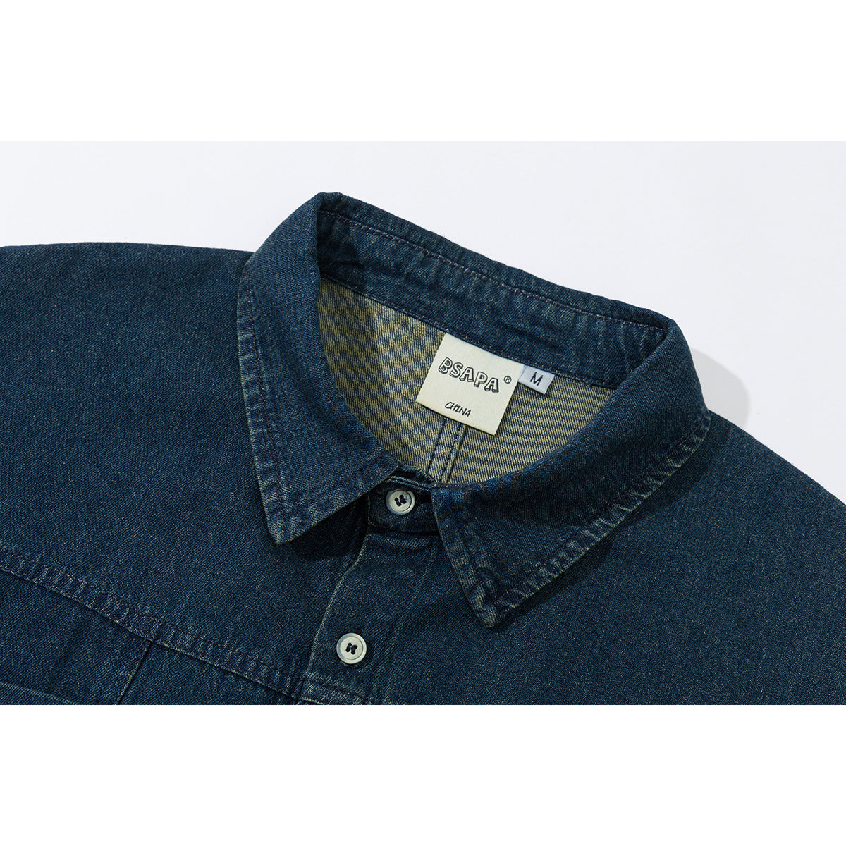 Close-up of a dark indigo denim shirt collar, top buttons, and sewn neck label.