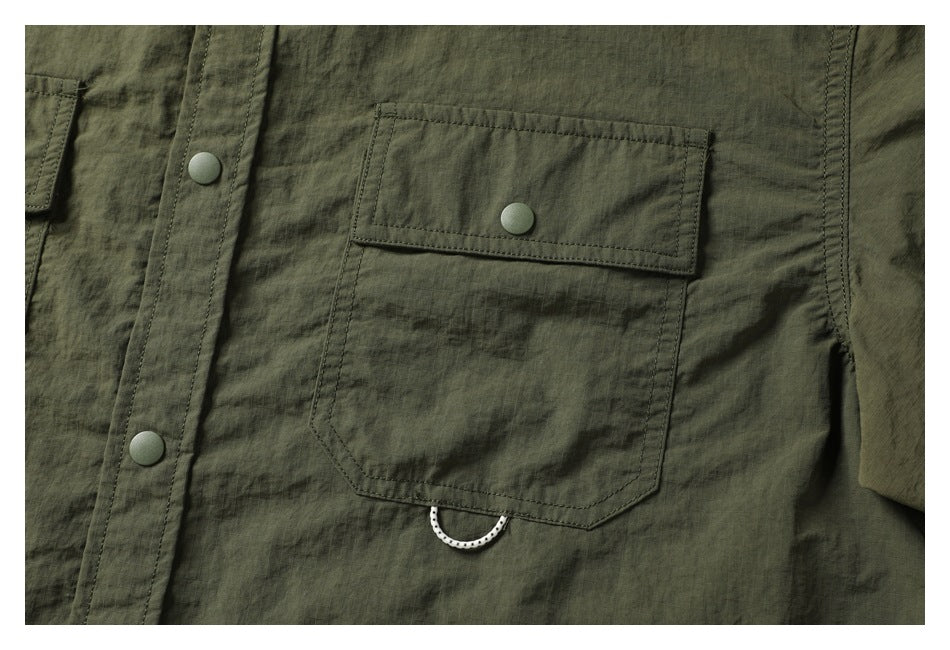 Close-up of the dark olive shirt's snap-button chest pocket, front placket, and small loop beneath the pocket.
