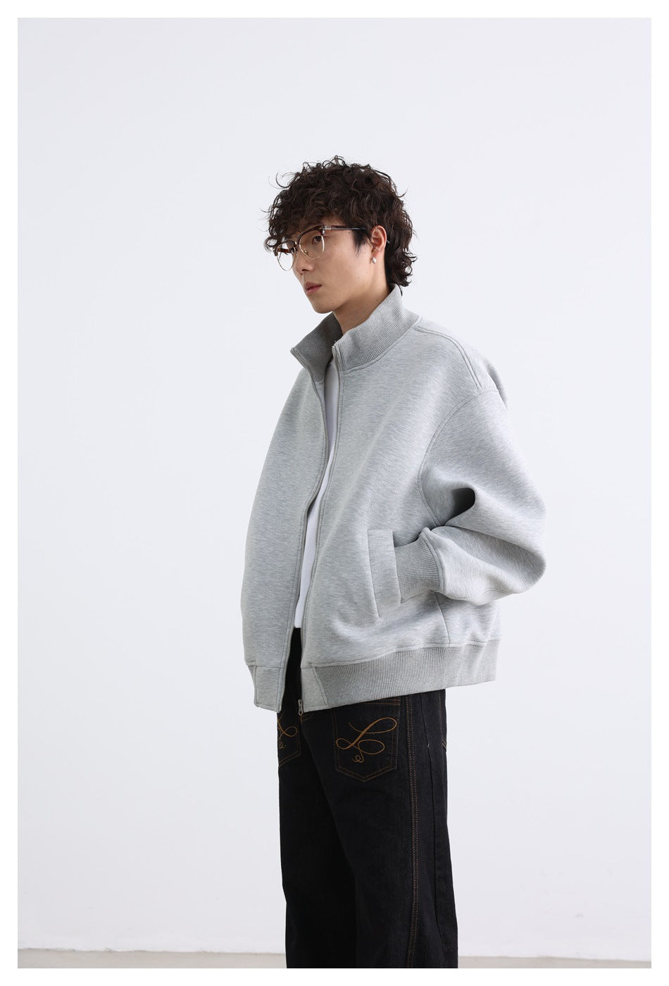 Side view of a model wearing a light gray zip-front jacket with a high collar and roomy sleeves.