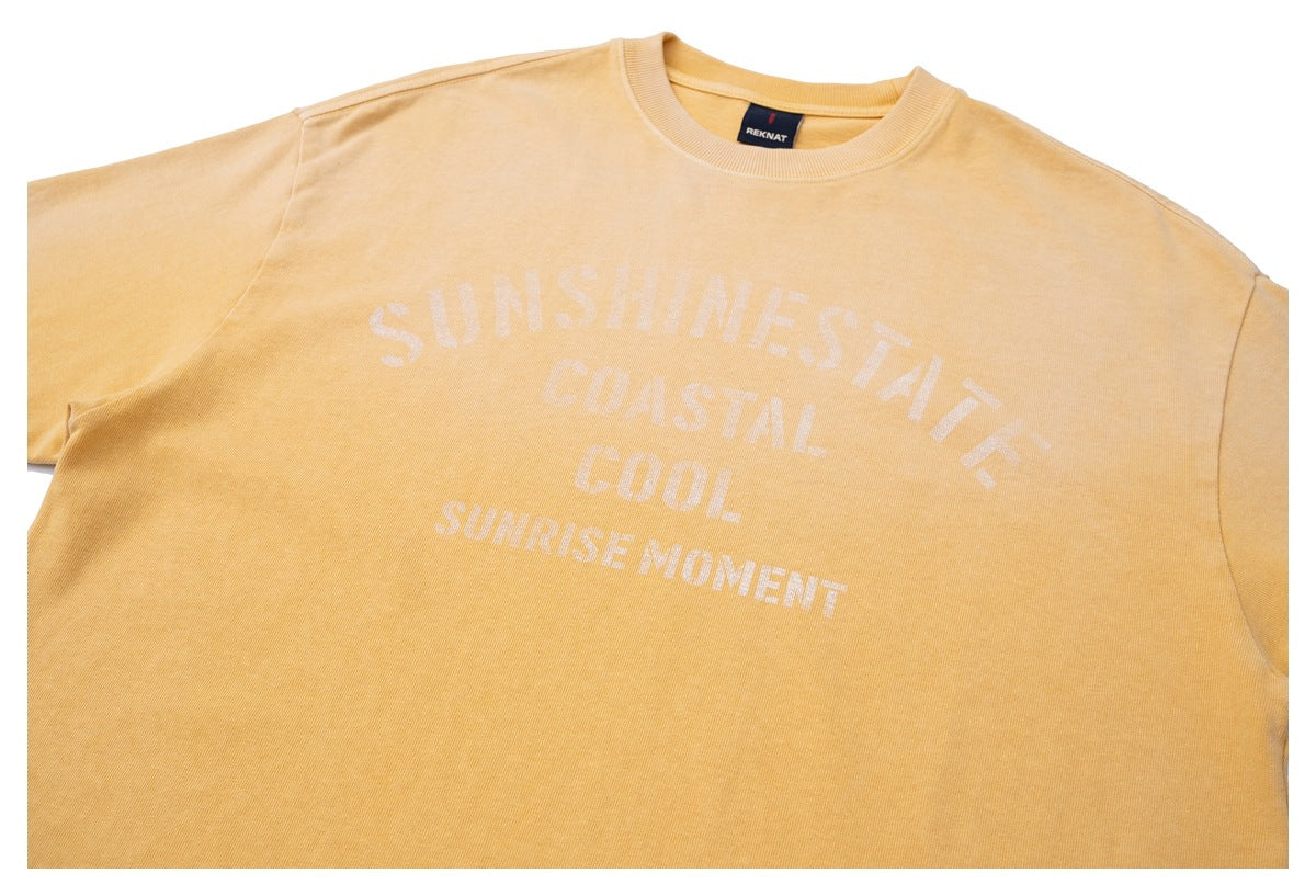 Cropped front view of a golden-yellow crewneck sweatshirt with pale lettering reading “SUNSHINE STATE COASTAL COOL SUNRISE