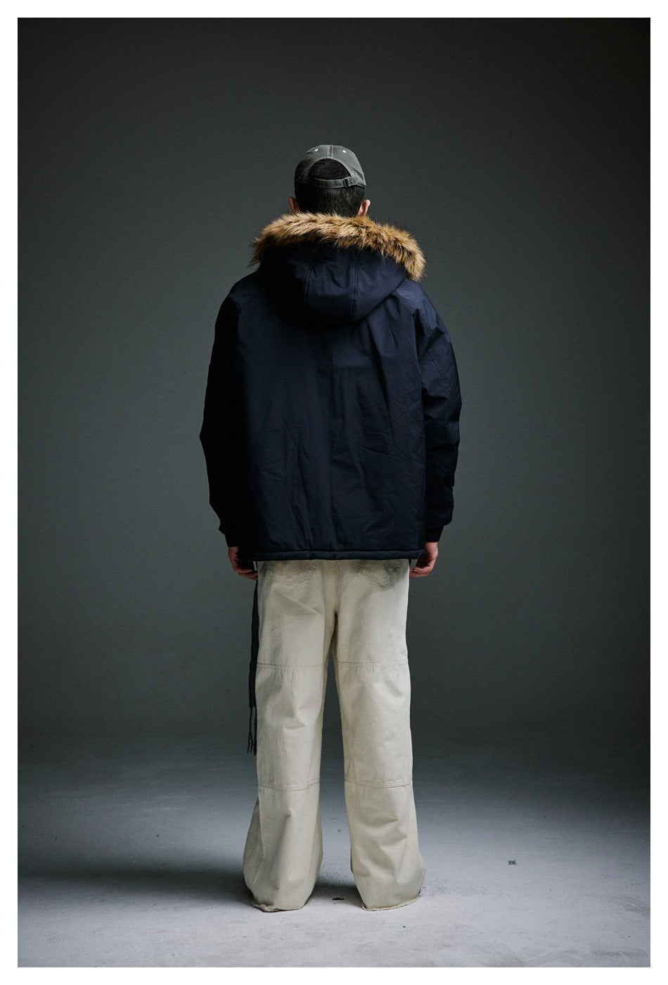 Back view of a model wearing a dark navy hooded jacket with faux fur-style hood trim and beige wide-leg pants