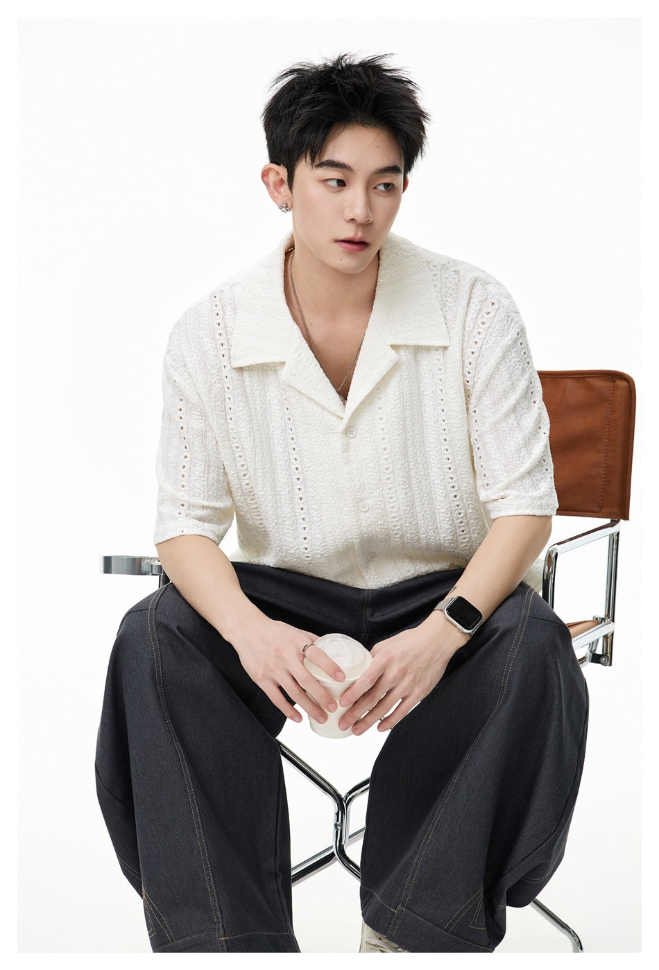 Seated model wearing an ivory textured short-sleeve button-up shirt with a notched collar.