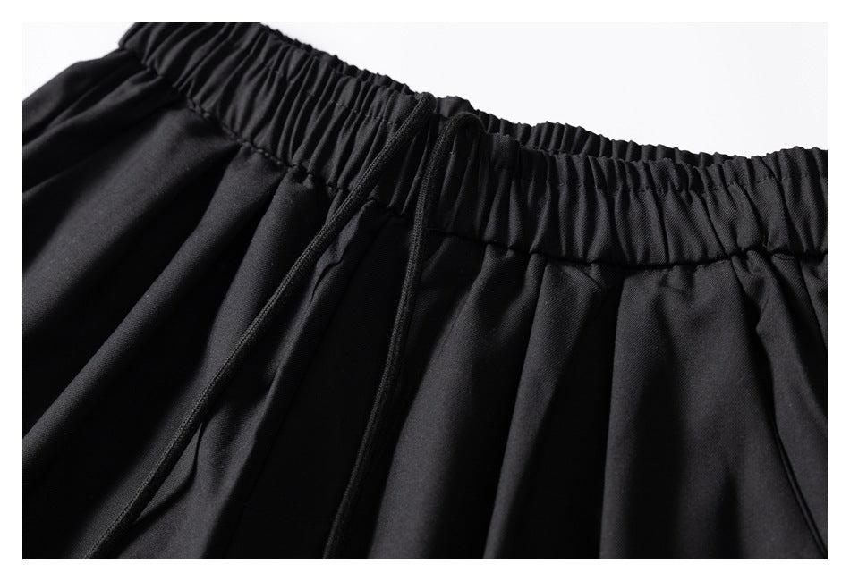 Close-up of the front of black trousers showing the elastic waistband, drawstring, and gathered fabric.