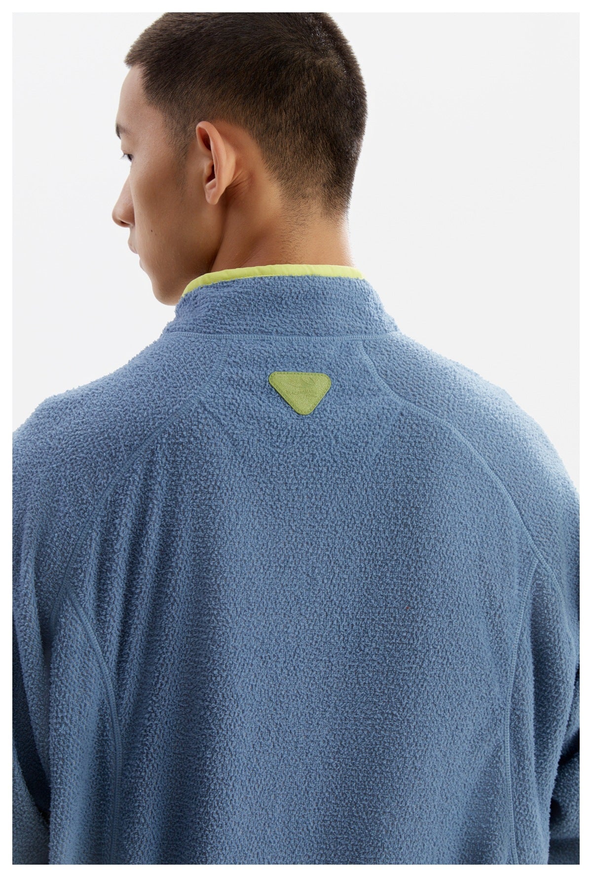 Back view of a model wearing a blue textured pullover with lime collar trim and a small green patch at the upper back.